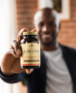 Blurry smiling man in black sweater holding out Solgar curcumin joint health supplement