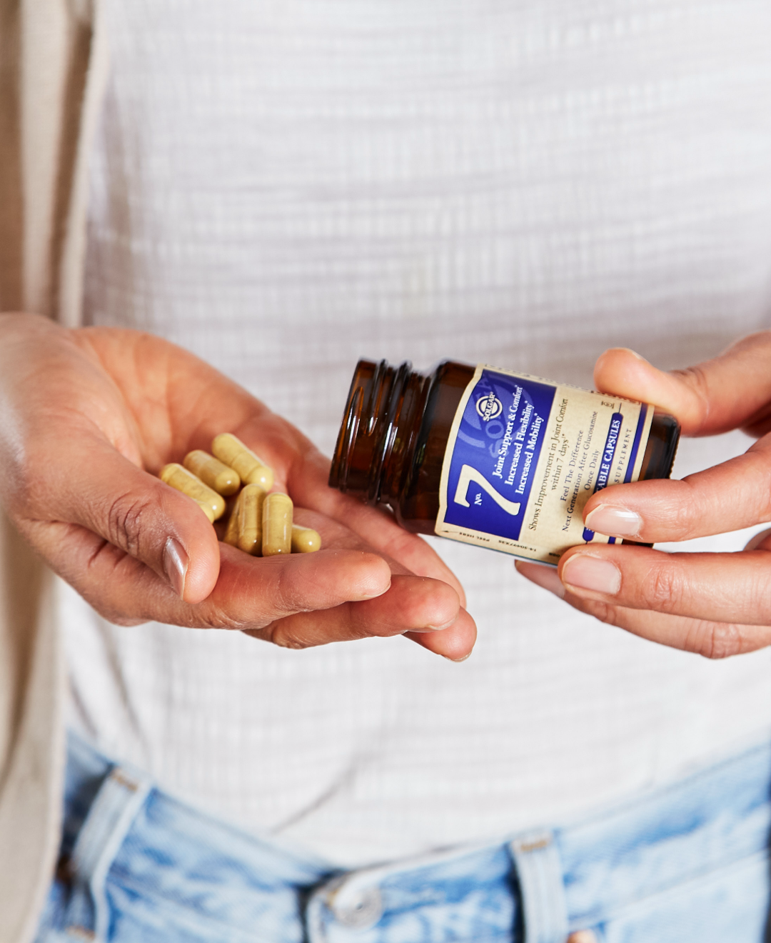 Torso shot of person with left hand holding Solgar number seven supplement pouring out capsules into right hand