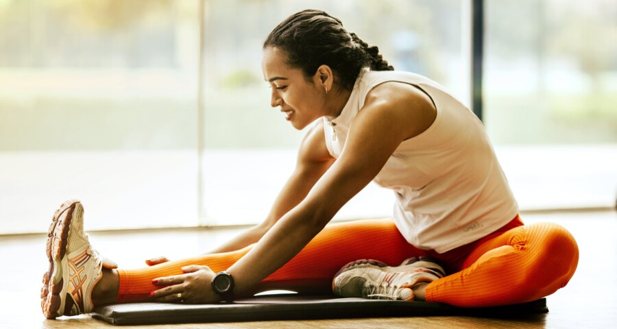 Woman in orange leggings stretching on black mat