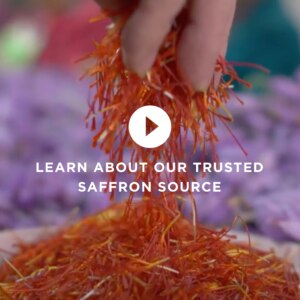 A hand pinches saffron from a dish. Text overlaid reads: "Learn about our trusted saffron source."