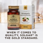 An image of a white box and amber glass bottle of Solgar Women's Balancing Formula tablets in a clean, white kitchen setting. The text on image reads, 