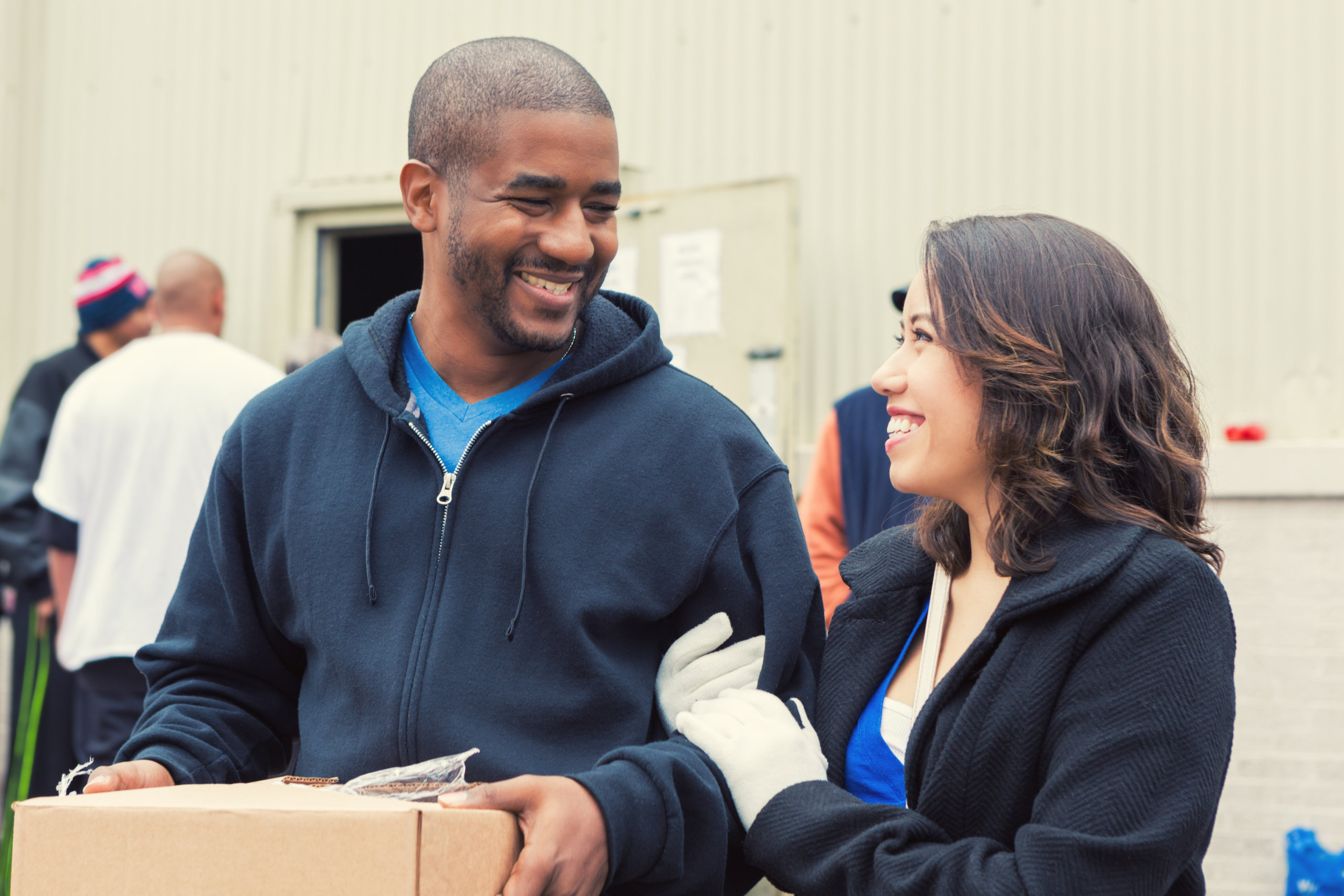 A man carrying a box and a woman, smiling at each other.