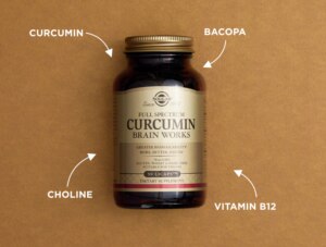 Product shot of Solgar Full Spectrum Circumin in an amberglass bottle against a textured brown background. Four white arrows on four separate corners point towards the bottle. Each arrow is labelled with a different ingredient: circumin, bacopa, choline, vitamin B12.