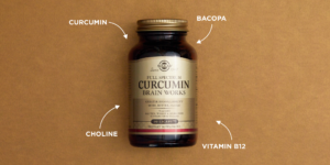 Product shot of Solgar Full Spectrum Circumin in an amberglass bottle against a textured brown background. Four white arrows on four separate corners point towards the bottle. Each arrow is labelled with a different ingredient: circumin, bacopa, choline, vitamin B12.