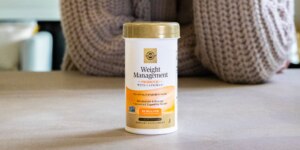 A bottle of Solgar Weight Management Probiotic on a beige countertop, in front of a woman wearing a grey knit sweater.
