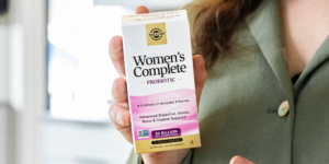 A closeup of a woman wearing a green shirt holding a box of Solgar Women's Complete probiotic