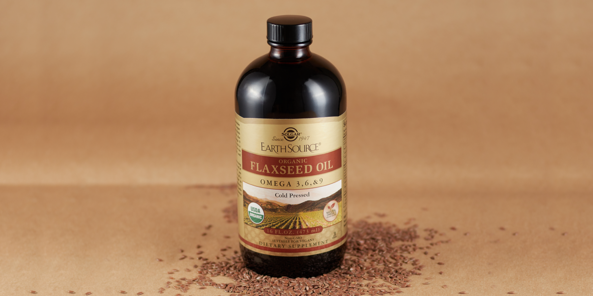 An amber glass bottle of Solgar Earth Source Flaxseed Oil, on a brown background with loose flax seeds around it.