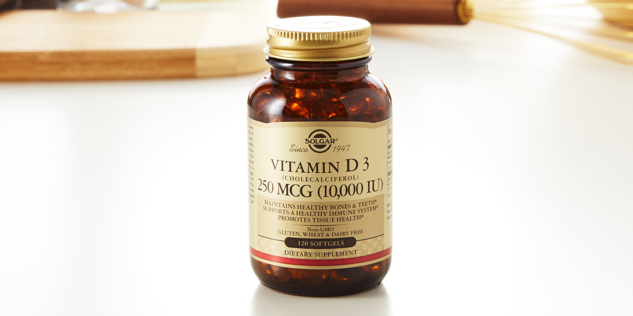 A closeup of a bottle of Solgar Vitamin D3 250mcg (10,000 IU) on a white background in front of kitchen items.