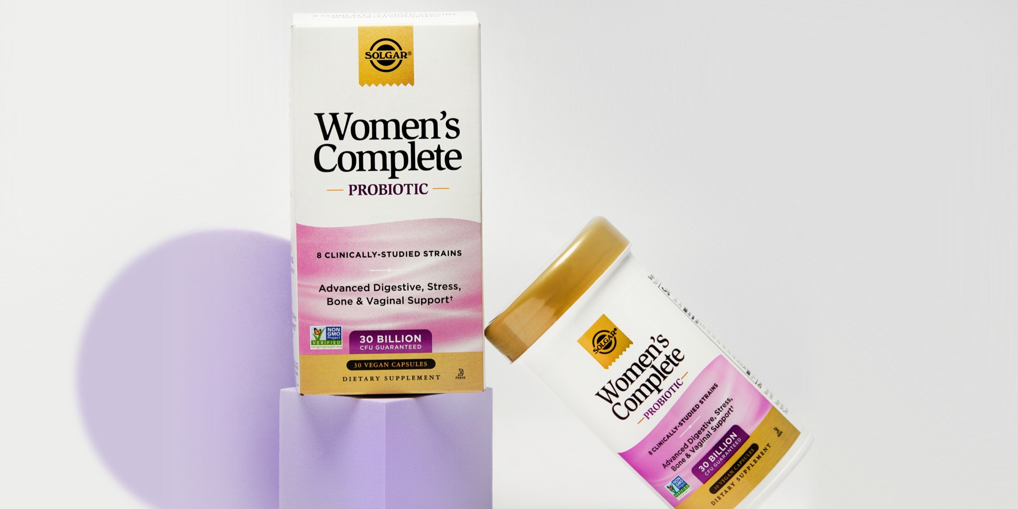 A box and bottle of Solgar Women's Complete probiotic sitting on a purple geometric shaped riser on a white background