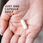 A woman's hand with a single capsule of Solgar One Daily Women's Mutli 50+ supplement in it to show size and scale. The image says, "Just one capsule daily".
