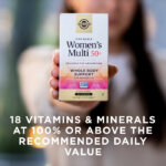 A woman holding a box of Solgar One Daily Women's Mutli 50+ supplement in her hand towards the camera. The box is in focus and the woman is blurred with the camera's depth of field. The image says, "18 vitamins and minerals at 100% or above the recommended daily value".