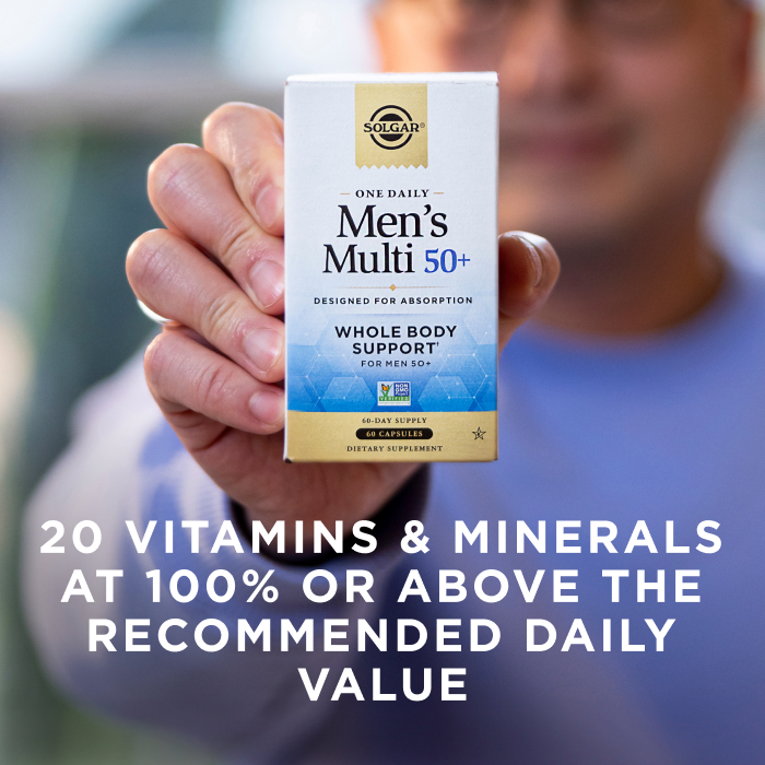 A man holding a box of Solgar One Daily Men's Mutli 50+ supplement in his hand towards the camera. The box is in focus and the man is blurred with the camera's depth of field. The image says, "20 vitamins and minerals at 100% or above the recommended daily value".