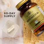 A bird's eye view of an amber glass bottle of Solgar One Daily Men's Multi 50+ supplement on a marble countertop. Beside the glass bottle is a single capsule showcasing the size and scale of the supplement. The image says, "60-day supply".