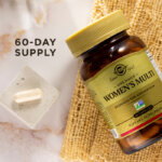 A bird's eye view of an amber glass bottle of Solgar One Daily Women's Multi supplement on a marble countertop. Beside the glass bottle is a single capsule showcasing the size and scale of the supplement. The image says, "60-day supply".