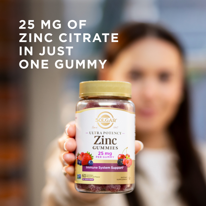 A woman holding a bottle of Solgar Ultra Potency Zinc Gummies towards the camera. The bottle is in focus but the woman is blurred with the camera's depth of field. The image says, "25 mg of zinc citrate in just one gummy."