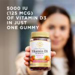 A woman holding a bottle of Solgar Ultra Potency Vitamin D3 Gummies towards the camera. The bottle is in focus but the woman is blurred with the camera's depth of field. The image says, "5000 IU (125 mcg) of Vitamin D3 in just one gummy."