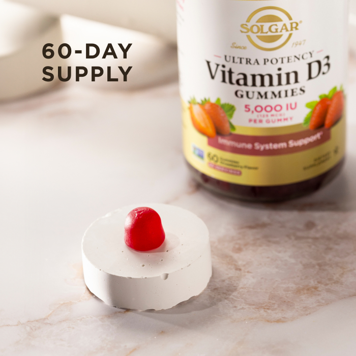 A single serving of Solgar Ultra Potency Vitamin D3 Gummies sitting on a white stone riser on a marble countertop. The gummy and riser is in focus, the bottle of vitamins is visible but blurred in the background. The image says, "60-day supply".