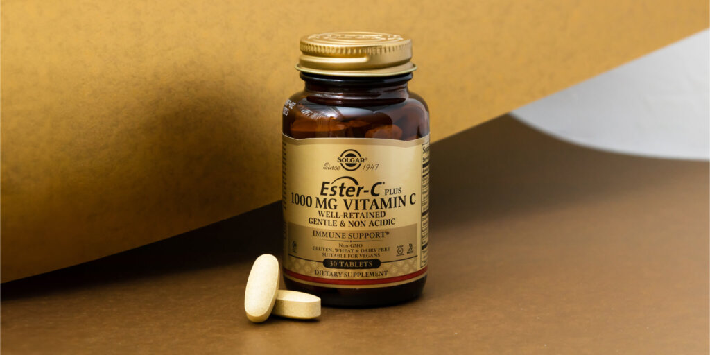 A bottle of Solgar Ester-C plus 1000mg tablets on a gold background. Two tablets are sitting outside of the bottle.