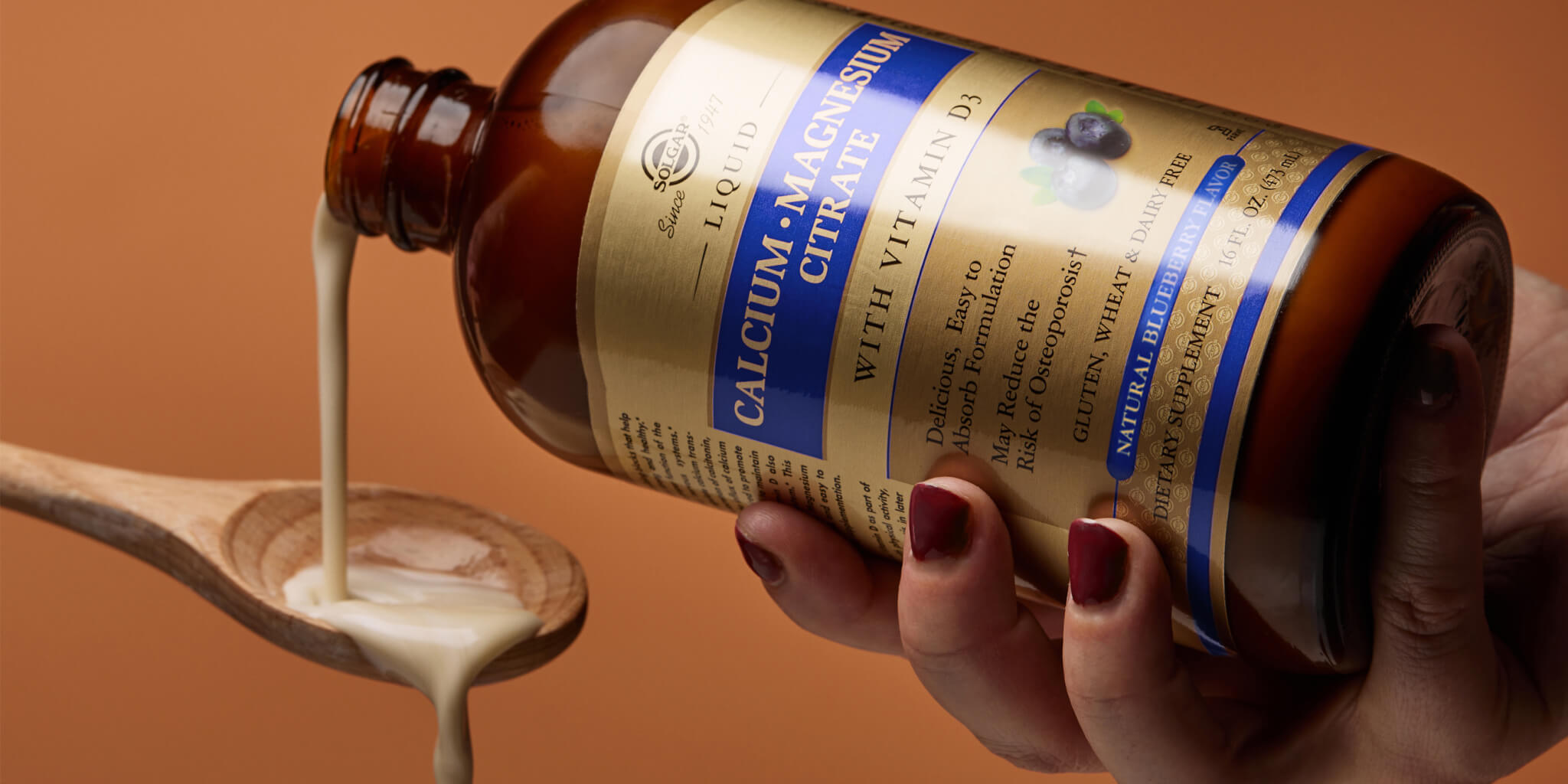 amber glass bottle with a beige liquid being poured onto a wooden spoon in front of a dark orange background