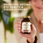 A bottle of Solgar's Bilberry Ginkgo Eyebright Complex Plus Lutein Vegetable Capsules being held in the foreground by a woman in the background. Text reads "promotes optimal eye health and vision support*"