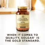 A bottle of Solgar's Calcium Magnesium Plus Zinc Tablets on a kitchen surface. Text reads "When it comes to quality, Solgar is the gold standard."