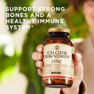 A woman holds a bottle of Solgar's Calcium Magnesium Plus Zinc Tablets in the foreground. Text reads "support strong bones and a healthy immune system"