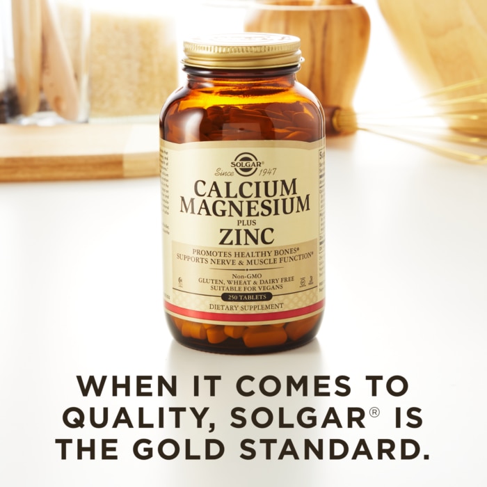 A bottle of Solgar's Calcium Magnesium Plus Zinc Tablets on a kitchen surface. Text reads "When it comes to quality, Solgar is the gold standard."