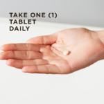 An outstretched hand holds a single Menopause Relief tablet against a light background. Text overlaid reads 'Take one tablet daily.'