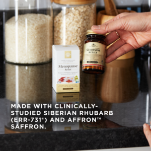 A hand holds an amber glass bottle of Menopause Relief Tablets in front of filled containers on a kitchen counter. Text reads: 'Made with clinically-studied Siberian rhubarb (ERr-731®) and affron™ Saffron.'