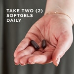 An outstretched hand holds two Ester-C® Plus Immune Complex softgels against a dark background. Text overlaid reads "Take two softgels daily."