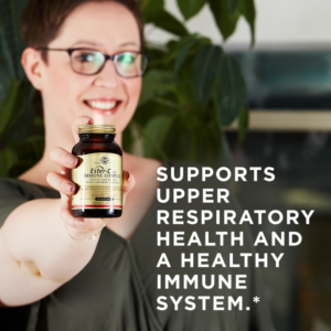 A smiling woman holds an amber glass bottle of Solgar's Ester-C® Plus Immune Complex softgels up to the camera. A text overlay reads: "Supports upper respiratory health and a healthy immune system.*"