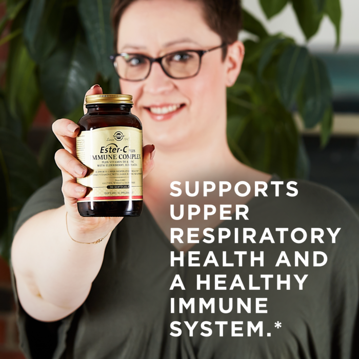 A smiling woman holds an amber glass bottle of Solgar's Ester-C® Plus Immune Complex softgels up to the camera. A text overlay reads: "Supports upper respiratory health and a healthy immune system.*"