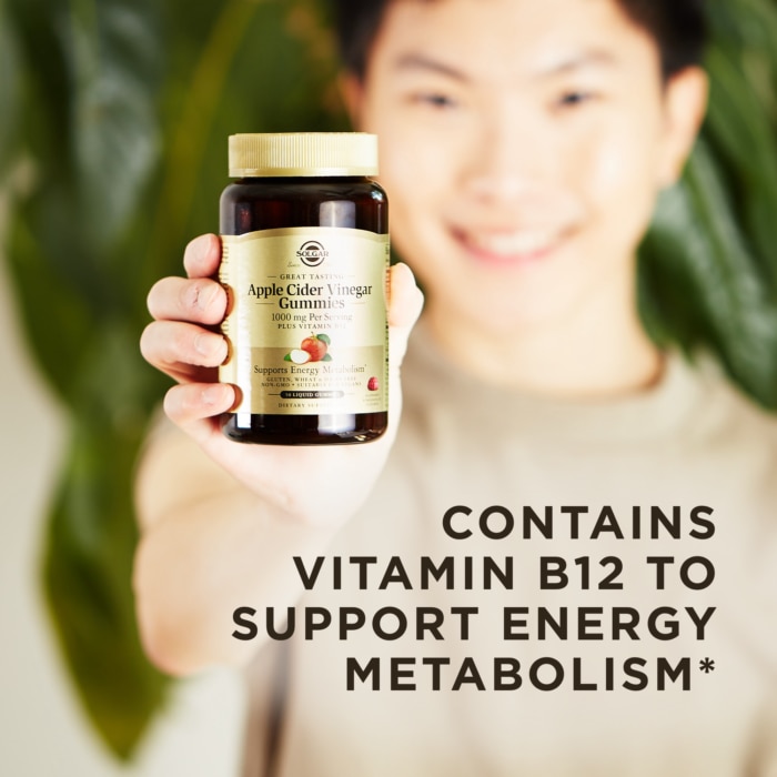 A smiling person holds an amber glass bottle of Solgar Apple Cider Vinegar Gummies up to the camera. A text overlay reads "Contains Vitamin B12 to support energy metabolism.*"