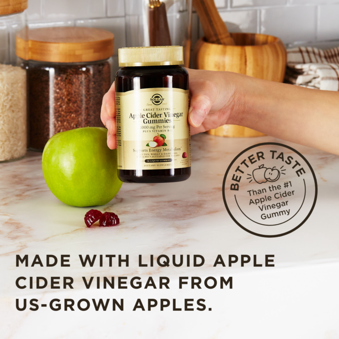 A hand holds an amber glass bottle of Solgar Apple Cider Vinegar Gummies above a kitchen surface next to an apple and some of the loose gummies. A text overlay reads "Made with liquid apple cider vinegar from US-grown apples." Another stamp on the image reads "Better taste than the #1 Apple Cider Vinegar Gummy."