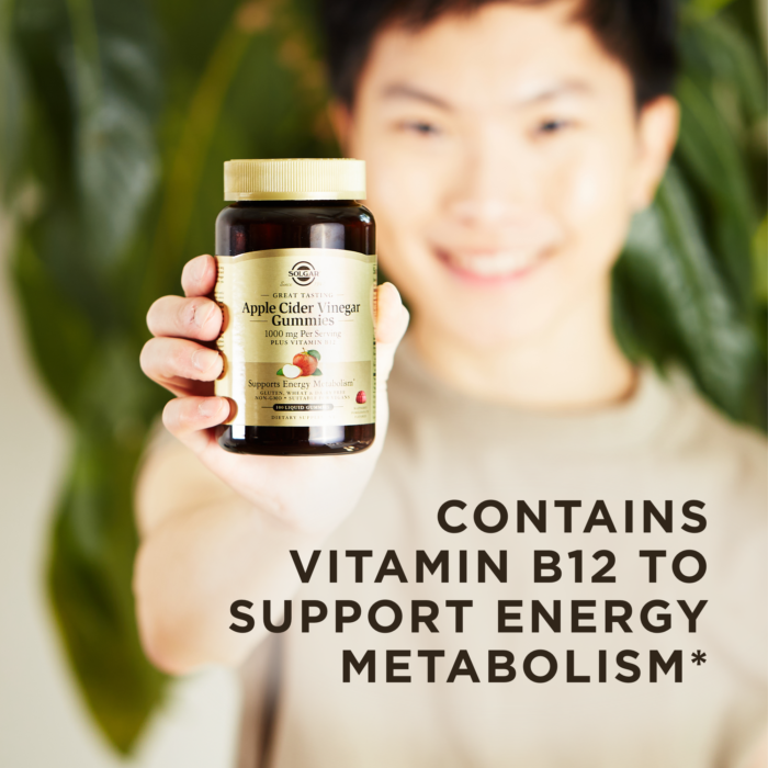 A smiling person holds an amber glass bottle of Solgar Apple Cider Vinegar Gummies up to the camera. A text overlay reads "Contains Vitamin B12 to support energy metabolism.*"