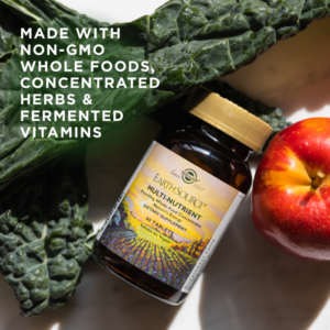 A bottle of Solgar's Earth Source® Multi-Nutrient Tablets sits next to apples and kale. Text reads "made with non-GMO whole foods, concentrated herbs, and fermented vitamins"