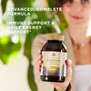A woman holds a bottle of Solgar's Earth Source® Multi-Nutrient Tablets up to the foreground, with text reading "advanced, complete formula. Immune support and daily energy support."