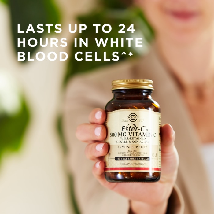 A bottle of Solgar's Ester-C® Plus 500 mg Vitamin C Vegetable Capsules (Ester-C® Ascorbate Complex) held up in a hand. Text reads "lasts up to 24 hours in white blood cells"