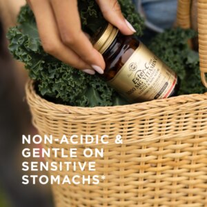A bottle of Solgar's Ester-C® Plus 1000 mg Vitamin C Tablets (Ester-C® Ascorbate Complex) being held by a woman in front of her. Text reads "non-acidic and gentle on sensitive stomachs"