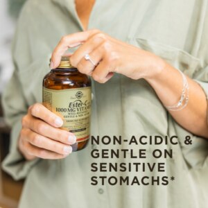 A bottle of Solgar's Ester-C® Plus 1000 mg Vitamin C Tablets (Ester-C® Ascorbate Complex) being held by a woman in front of her. Text reads "non-acidic and gentle on sensitive stomachs"