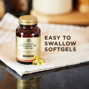 A bottle of Solgar's Evening Primrose Oil 1300 mg Softgels on a cloth with two of the softgels loose next to it. Text reads "easy to swallow softgels"