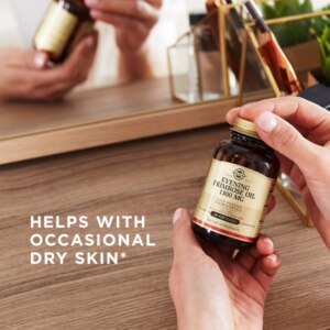 A bottle of Evening Primrose Oil 1300 mg Softgels being held in front of a mirror with two hands. Text reads "helps with occasional dry skin"