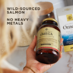An amber bottle of Solgar's Wild Alaskan Full Spectrum™ Omega Softgels with a golden lid. Text reads "no fishy aftertaste, added rosemary, sage and thyme extracts.