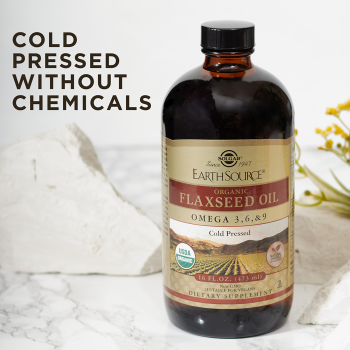 A bottle of Solgar's Earth Source® Organic Flaxseed Oil sits on a marble surface, with text reading "100% unrefined, cold-pressed without chemicals"