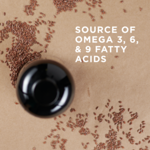 A view of an open bottle of Solgar's Earth Source® Organic Flaxseed Oil from above. Flaxseeds are scattered around on a coral-colored surface. Text reads "source of omega 3, 6, and 9 fatty acids"