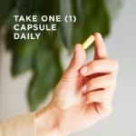 A single vegetable capsule of Solgar's B-Complex "100" supplement is held between the finger and thumb of a hand. Text reads "take one capsule daily"