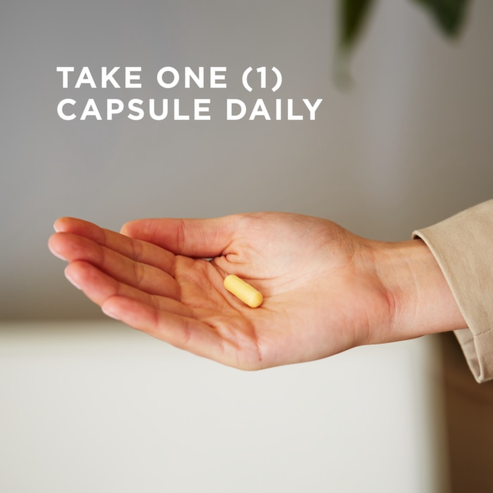 A single vegetable capsule of Solgar's B-Complex "100" supplement is held in the palm of a hand. Text reads "take one capsule daily"