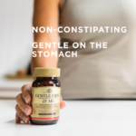 A bottle of Solgar's Gentle Iron Vegetable Capsules held on a counter by a woman. A text overlay reads: "Non-constipating. Gentle on the stomach."