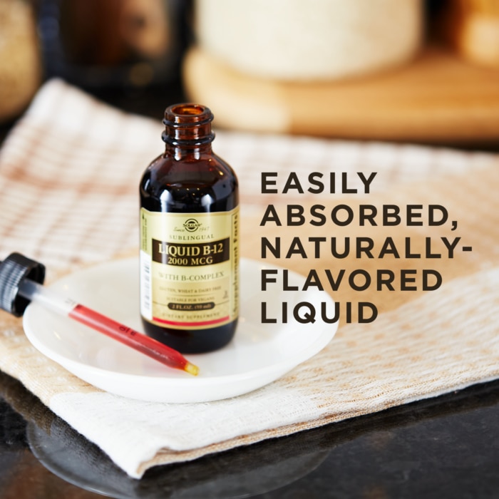 A bottle of Solgar's Sublingual Liquid B-12 2000 mcg with B-Complex, with the dropper lid removed and placed next to it, on a white dish. Text reads "easily absorbed, naturally flavored liquid"