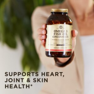 A woman holds up Solgar's Omega-3 Fish Oil Concentrate Softgels in an amber glass bottle. Text reads 'supports heart, joint, and skin health"